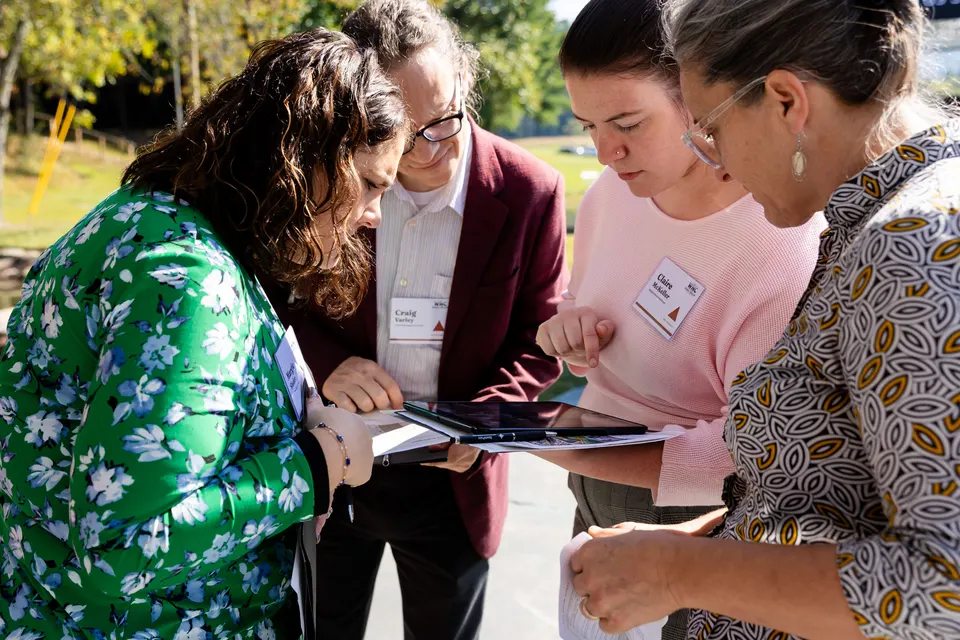 Four attendees crowd around a tablet, talking through a simulator scenario together