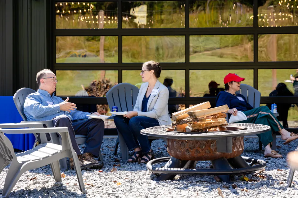 Attendees talk in Adirondack chairs around a fire pit outside the barn