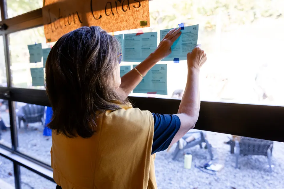 An attendee pins a card to a window covered in Connection to Action cards