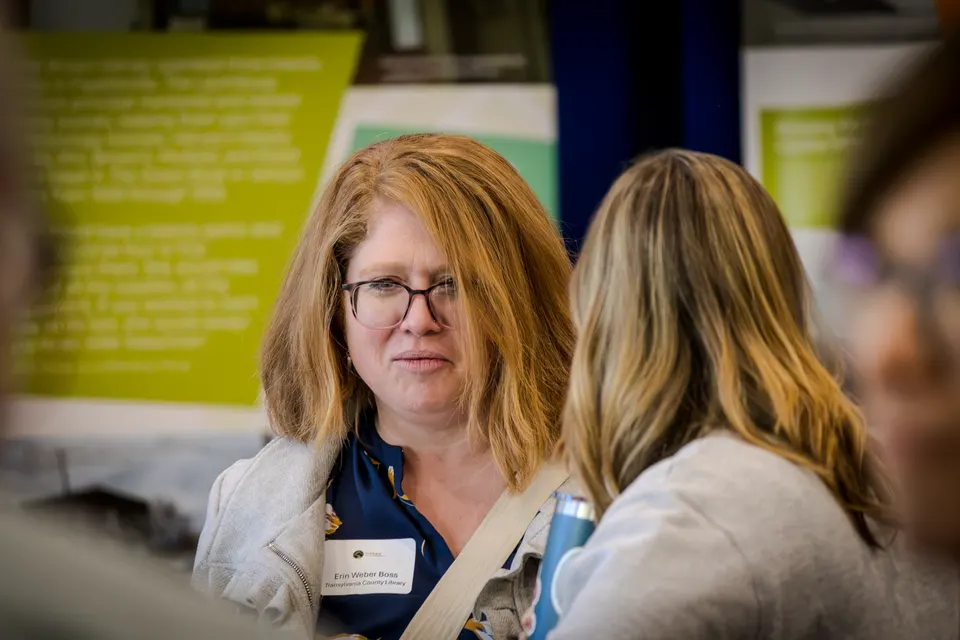 A woman with glasses and red hair in close conversation with another attendee.