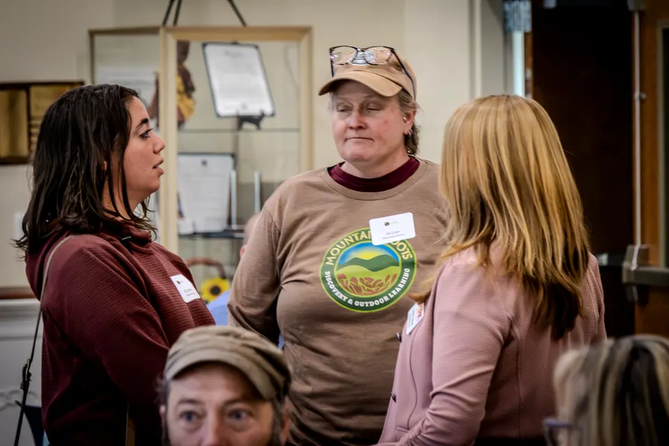 Three women in conversation in front of a wall of framed history displays.
