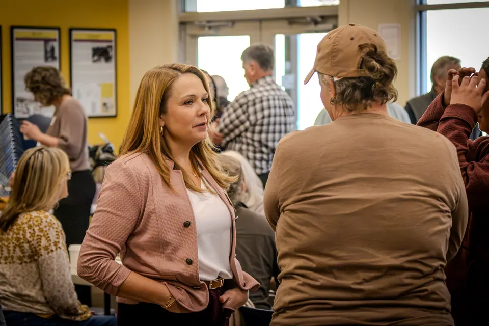 The woman in the pink cardigan in the middle of a busy room of conversations.
