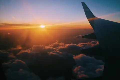 Sunset over the clouds from an airplane window, the wing in silhouette.