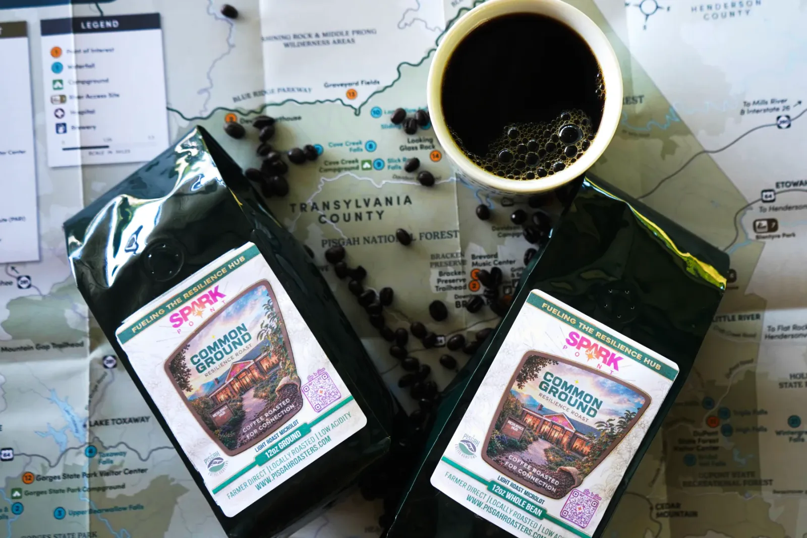 Two bags of Common Ground Resilience Roast and a cup of coffee arranged over a map of Transylvania County.
