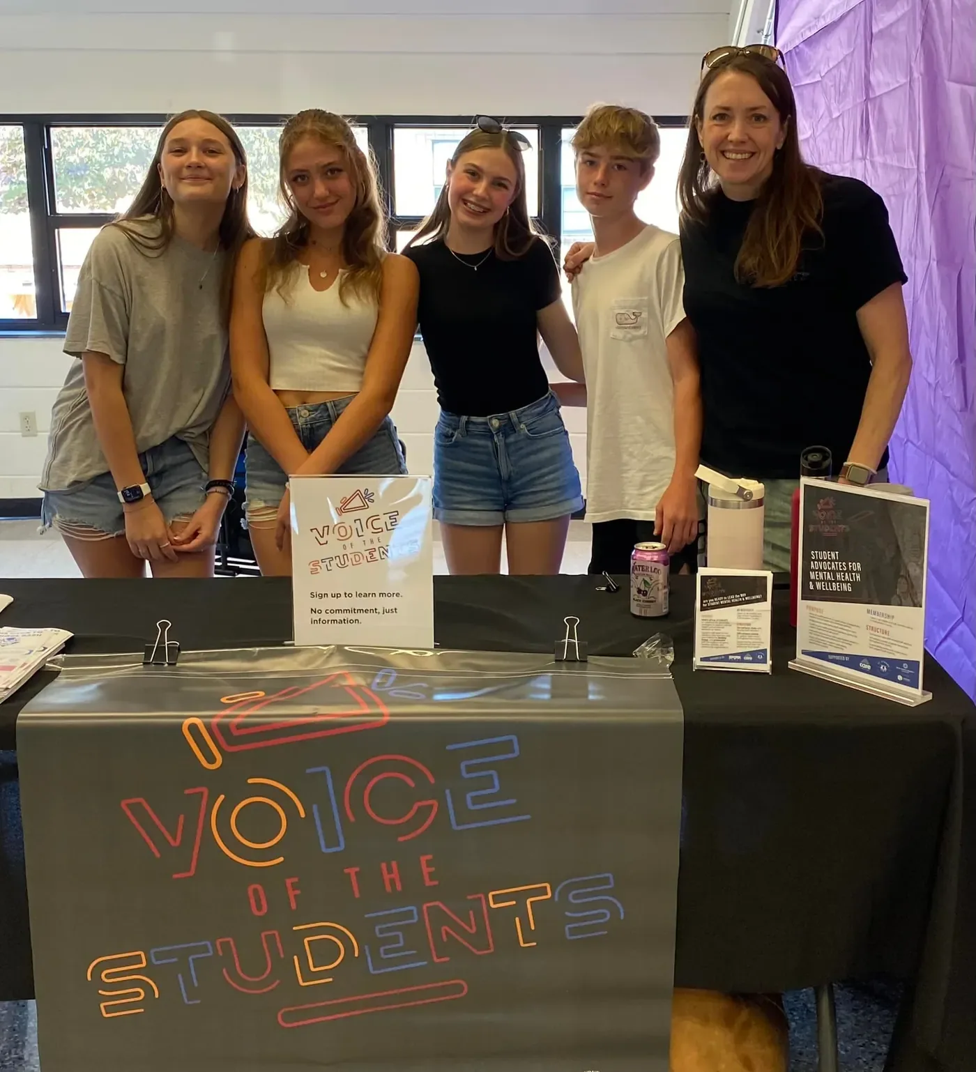 Four students and an adult volunteer at a Voice of the Students sign-up table.