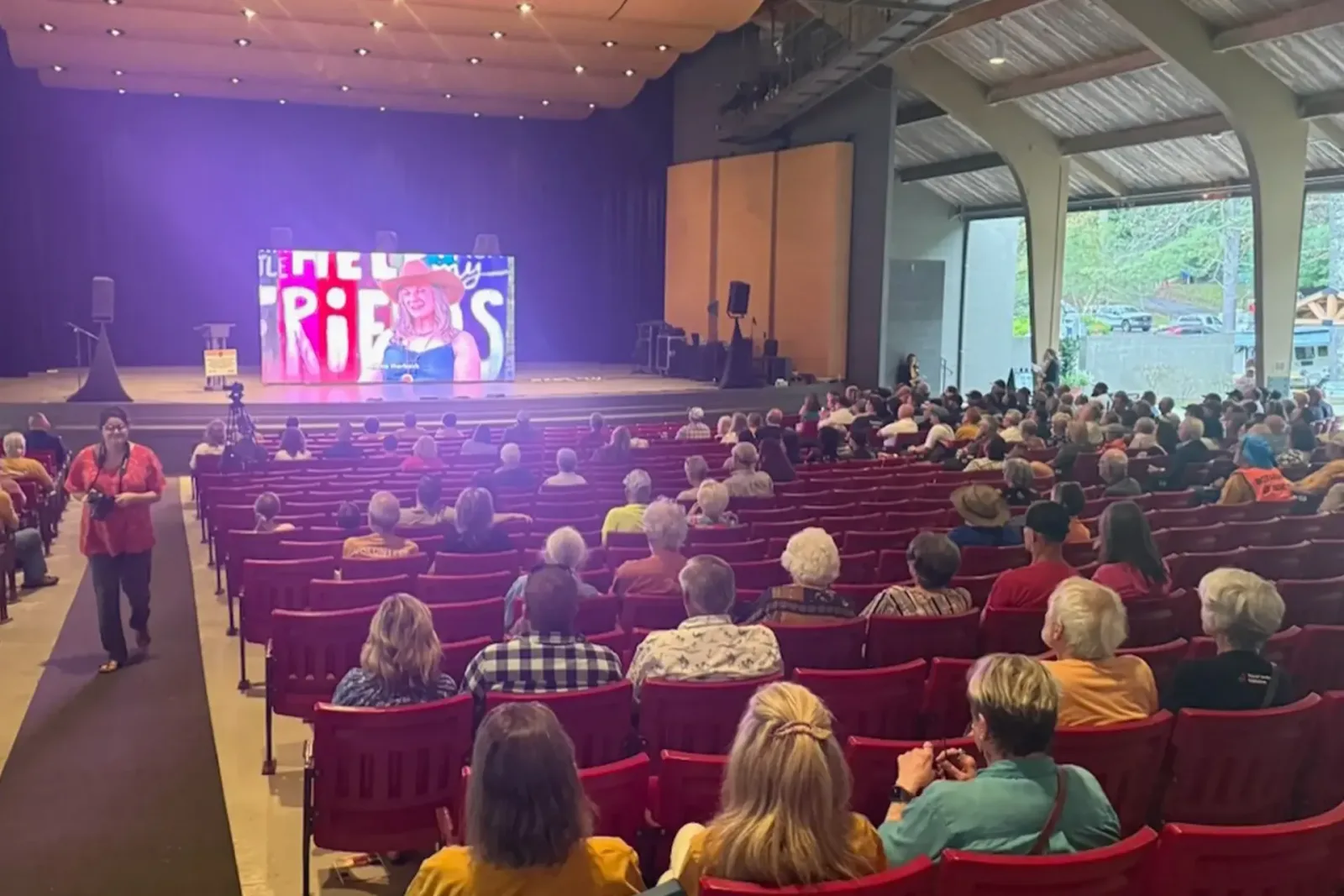 An audience fills an open-air auditorium as a resident's story plays on the big screen at Helene: One Year of Healing.