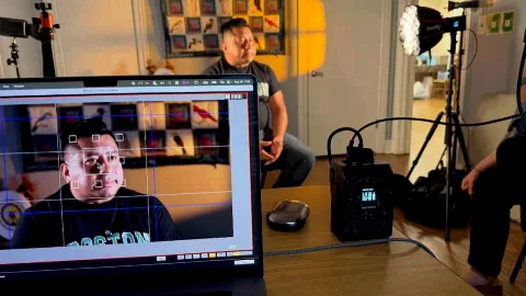 A storyteller seated in a living room, his face on the recording monitor in front.